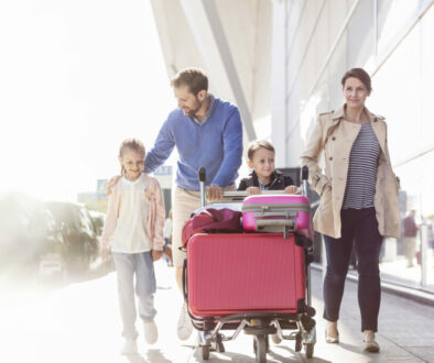 Family with luggage cart walking outside airport