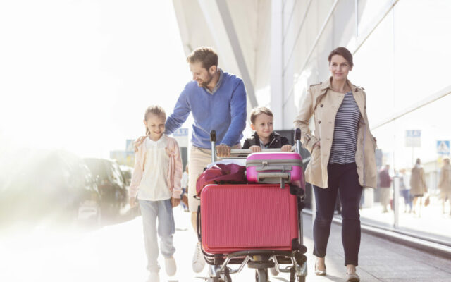 Family with luggage cart walking outside airport